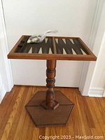 Full view of the backgammon table showing solid wood pedestal base and foldable playing surface with bag of game pieces on top.