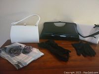 Photo showing two handbags (white and black), floral scarf, black ruched gloves, and plain black gloves on wooden surface.