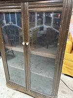 Front view showing glass doors, round metal knobs, and notable heavy wear on dark brown wood finish.