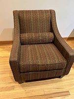 Front view of a modern swoop armchair with chenille pinstripe upholstery and matching bolster pillow on hardwood floor