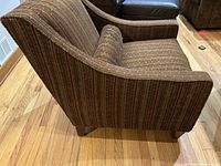 Side view of modern armchair showing swoop styled arm and pinstripe chenille fabric upholstery.