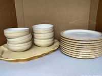 Yellow ceramic serving platter, nine caramel striped Denby plates (stacked), and six caramel striped Denby bowls (stacked); plates and bowls show signature caramel horizontal stripes on cream ceramic.