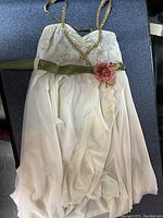 White costume dress with gold embellishments and flower sash laid on blue surface.