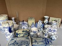 Overall photo showing all items in the lot including tins, ceramic dishes, figurines, and decorative pieces with Dutch windmill and village themes.
