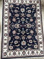 Full view of the rectangular Oriental rug showing midnight blue field with detailed floral and vine motifs bordered by a cream band with floral designs.
