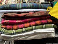 Stack of folded fleece fabric pieces in plaid and solid colors including green, brown, red, pink and white.