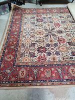 Close-up corner view showing the red border with floral and geometric motifs and part of the beige central field with detailed floral patterns.