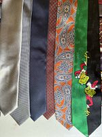 Close-up photo showing 7 neckties in different colors and patterns including solid grey, blue gradients, paisley, and cartoon motifs.