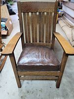 Front view of the oak mission-style armchair showing the slatted wood back and brown leather seat cushion.