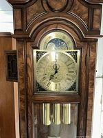 Front view of entire clock case showing hood, dial and visible weights behind glass.