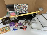 Overview of all items on brown cardboard background showing organizers, scissors, hole punchers, bookends, lamp, pencil sharpener, yardstick, clipboards, and stationery.