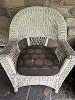 Front view of one white wicker outdoor chair with brown multicolored circular pattern cushion, showing woven wicker details and cushion pattern.