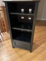 Front view of the black cabinet showing three shelves and cable management holes.