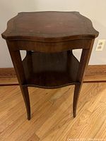 Front view of vintage tiered accent table showing curved edges, tapered legs and two-tier design