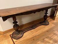 Side view of the solid dark hardwood console table showing its turned pedestal legs and curved stretcher base with circular feet