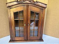 Solid wood wall cabinet with double glass paneled doors and brass knobs, front view