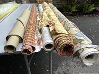 Six rolls of upholstery fabric on folding table, various patterns and colors visible