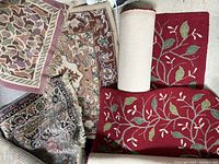Flat view of several rugs including red floral rugs and oriental rugs spread out; shows pattern and condition.
