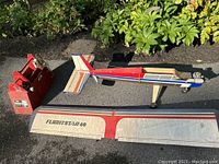 Full view of RC plane body, detachable wing labeled Flightstar 40, and red remote controller placed on ground outdoors near plants.