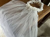 Close-up of the veil showing white tulle fabric attached to floral and bead decorative headpiece with white flowers.