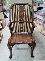 Full front view of dark hardwood Windsor armchair highlighting curved armrests, carved back splat, and cabriole legs.