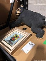 Photo showing ceramic bear figurine lying next to framed painting and auction tag