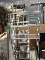 Full view of white metal over-the-toilet style shelf with multiple wire shelves and curved silver bar on top.