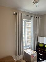 Close-up of light beige/taupe blackout curtains hung on black curtain rod with white finials.