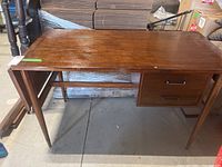Front view of wooden desk showing rectangular top, tapered legs, and two drawers on the right side.