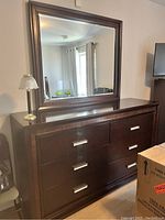 Front view of dark brown wooden dresser with attached mirror, six drawers with silver handles visible.