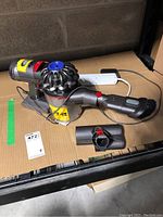 Dyson V7 Trigger handheld vacuum with charger, placed on cardboard surface.