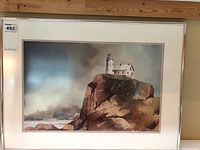 Full view of framed watercolor painting showing lighthouse on rocky cliff with sky and ocean background.