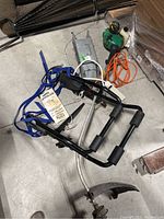 Photo showing Thule bike carrier with blue straps and manual, gas weed eater/trimmer, orange extension cord, and part of animal trap and vine trellises on warehouse floor.