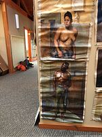 Both paintings hanging one above the other showing female nude on top and male nude below, rolled canvas with visible creases and paint damage.