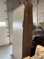 Photo showing the full rectangular hot tub lid standing upright with the brown textured sides visible and the light-colored cushioned top edge partly visible below the sides.