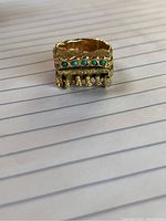 Front view of ring on lined paper showing textured gold band and five turquoise stones