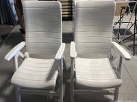 Front view of two white folding plastic lawn chairs showing slatted seat and backrest with armrests.