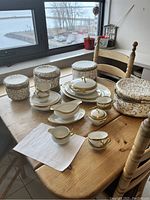 Overview of white porcelain gold-trimmed dinnerware including cups, saucers, plates, serving dishes, cream pitcher, sugar bowl, gravy boat, and covered dish