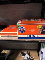 Two orange-and-white Lionel boxes on a shelf: left TrainMaster Command Set, right ZW Multi-Watt Transformer.