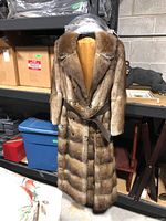 Full-length view of long mink coat on display, showing overall length, fur pattern, and satin lining.