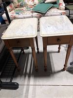 Two matching wooden side tables with white marble tops, each with one drawer and turned legs, standing side by side on floor.