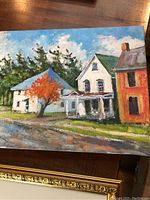 Painting showing street scape with white, red, and blue-roofed houses, tree with orange leaves in foreground, visible brush strokes.
