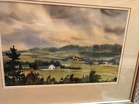 Framed watercolor painting showing rural Ontario landscape with fields, buildings, and hills under cloudy sky.