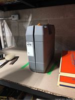 Grey hard plastic carrying case with a handle, labeled Ryobi Hammer Drill, closed and standing upright.