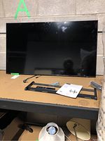 Samsung flat screen TV placed on table with black plastic stand legs and power cord nearby, along with wall mount parts.