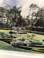 Close-up photo showing the garden scene with manicured hedges and urns under natural light.