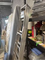 Full view of 6 foot aluminum step ladder leaning in storage area.