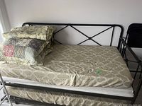 Overall view of black metal daybed with fitted sheet, quilt and shams piled on top