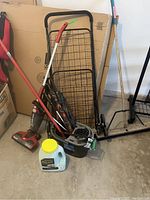 Photo of various utility items including upright vacuums, folding grocery cart, mop, bucket, and container with vacuum seal bags