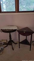 Two wooden accent tables side by side: round pedestal table with lace doilie on top and triangular table with drop sides.